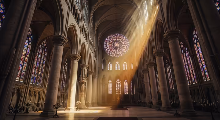 Colored light from a stained-glass window streaming into the dark stone interior of a Gothic cathedral.