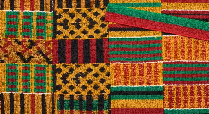 A close-up detail of a vibrant African Kente cloth, showing intricate woven patterns and symbolic colors.